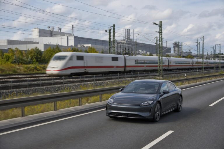 Elektromos autó német autópályán vasútvonal és ipari háttér mellett