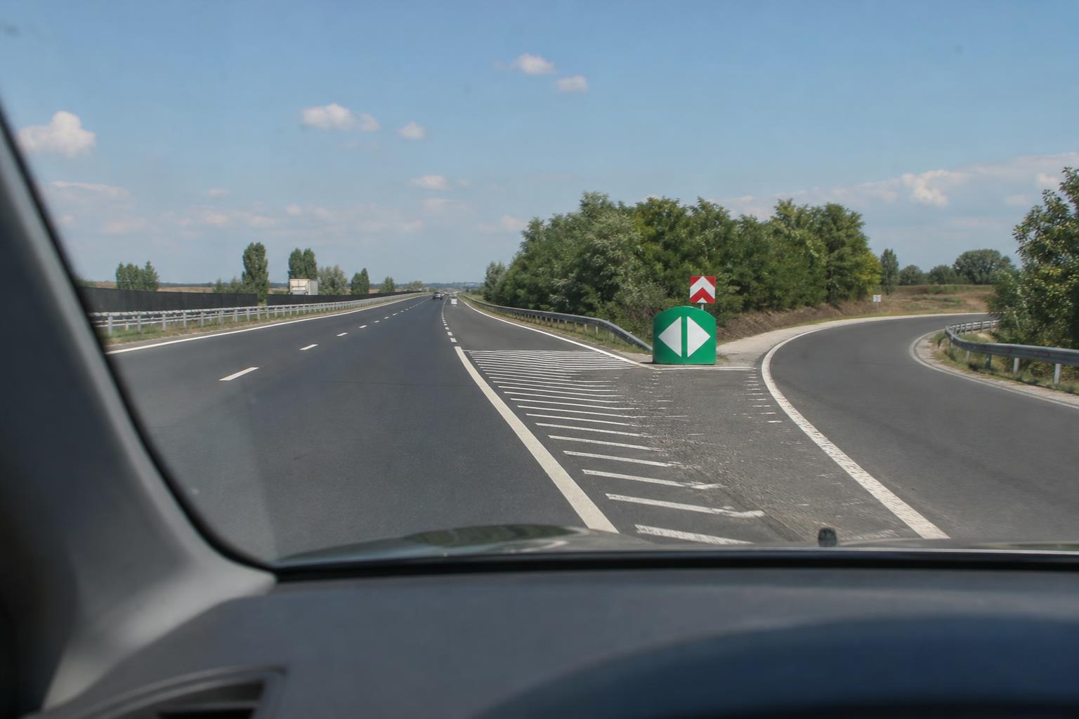 Autó halad tovább az autópályán egy eltévesztett lehajtó után, a kijáratot jelző táblával