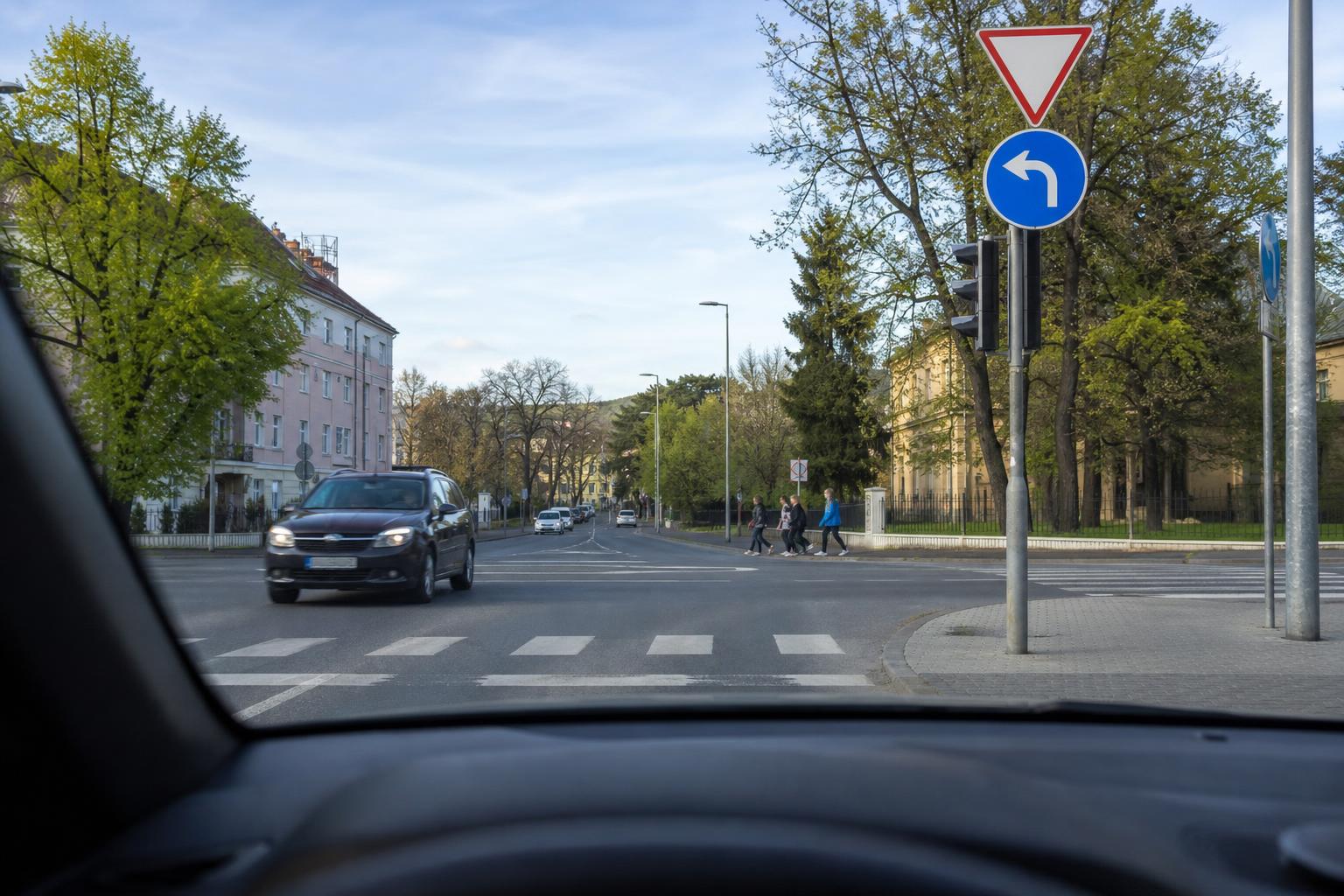 Balra kanyarodásra váró autó egy kereszteződésben, szemből egyenesen haladó járművel és zebrával