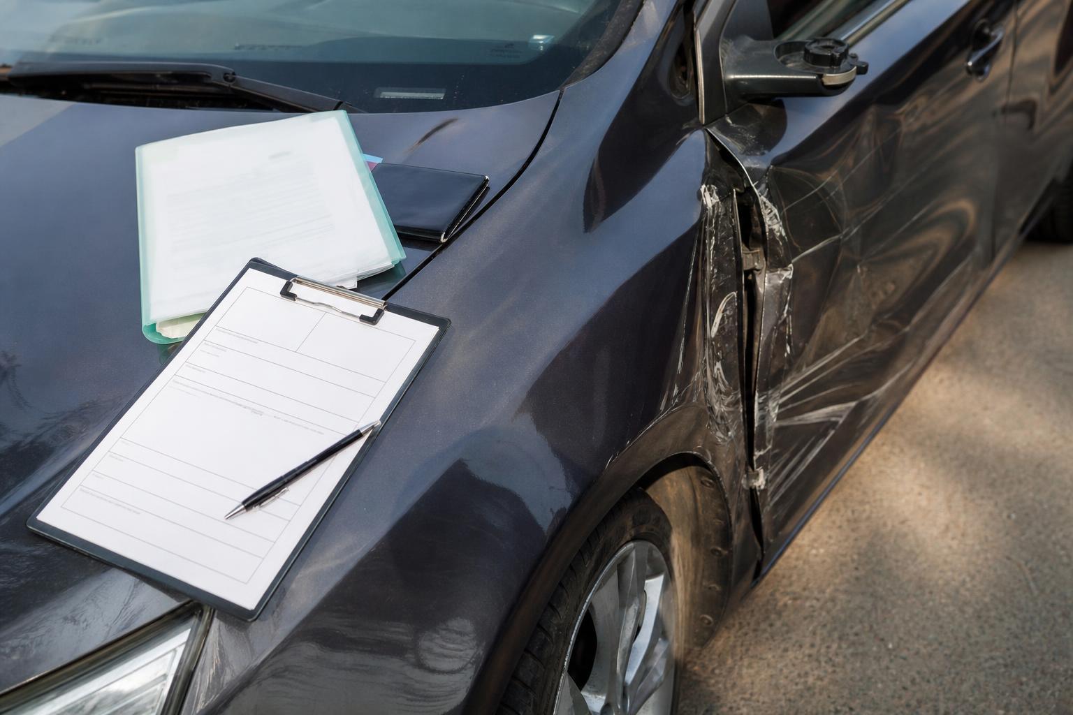 Sérült autó és kárbejelentéshez használt dokumentumok a jármű motorháztetején