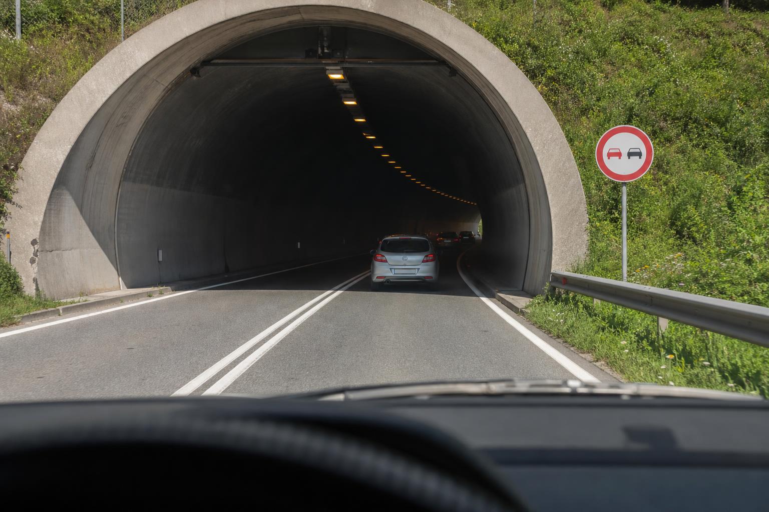 Autó közeledik alagút bejáratához előzést tiltó jelzéssel és jól látható útburkolati jelekkel