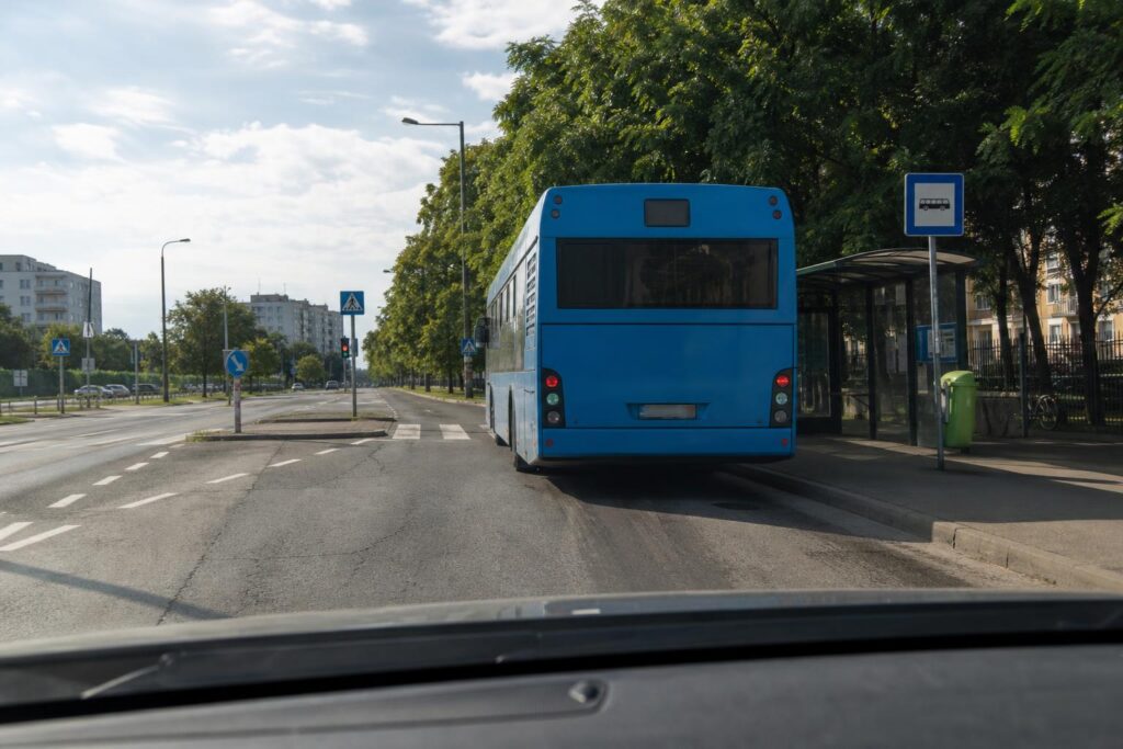Városi buszmegállóban álló autóbusz, amely részben takarja a közeli gyalogosátkelőhelyet