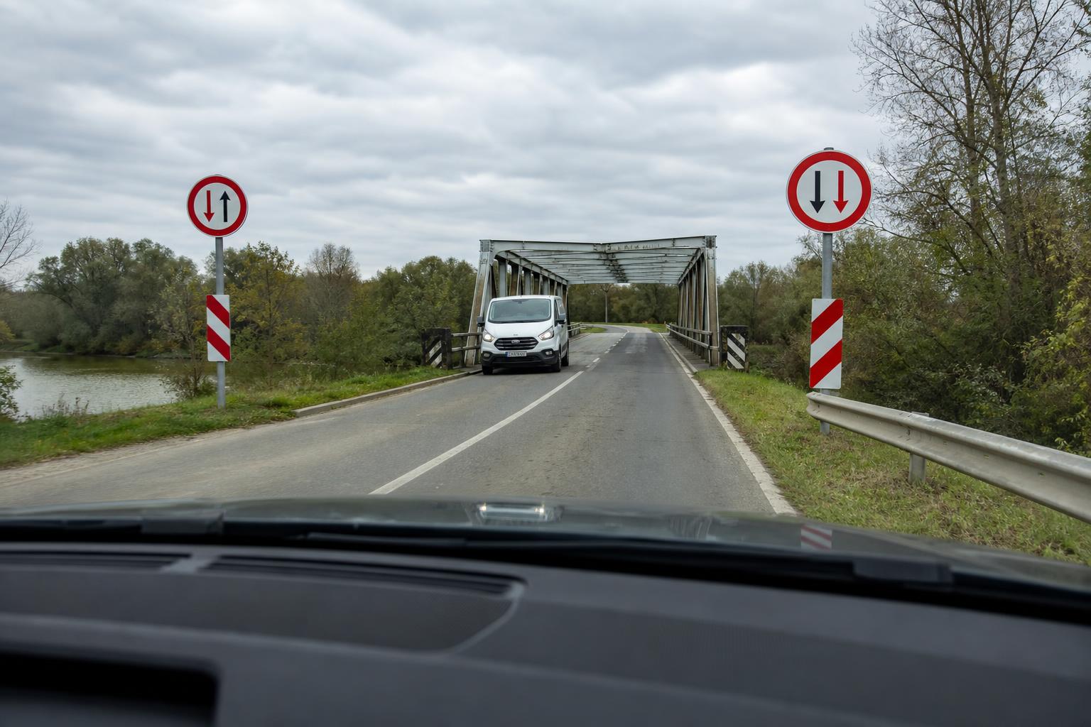 Keskeny hídra érkező autó szembejövő járművel és elsőbbséget jelző közúti táblákkal