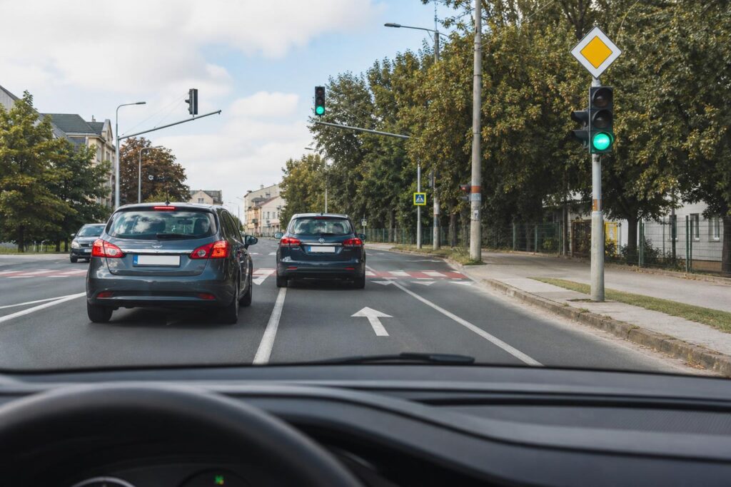 Autó előz egy másik járművet jelzőlámpás, főútvonalon fekvő kereszteződésben