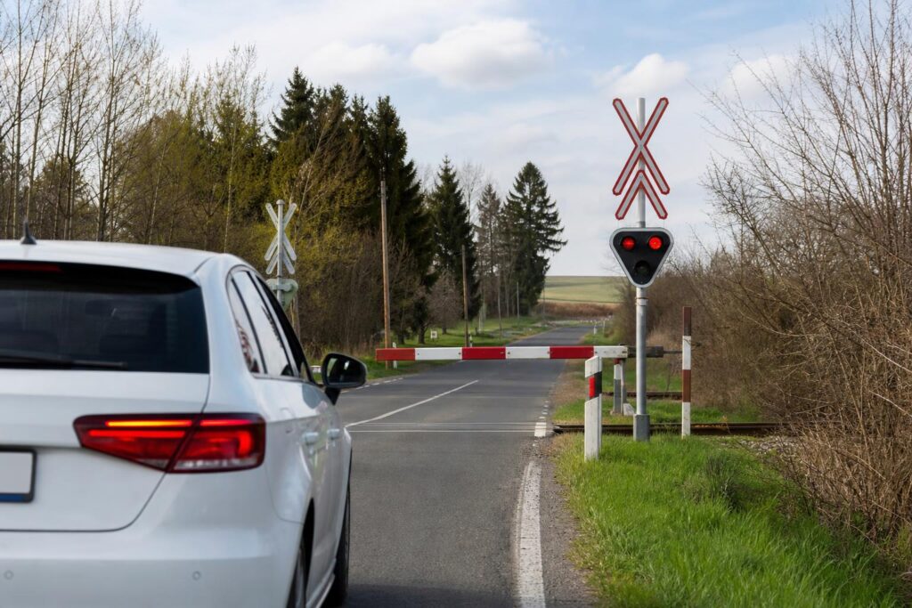Autó közelít vasúti átjáróhoz leengedett sorompó és villogó fényjelzés mellett