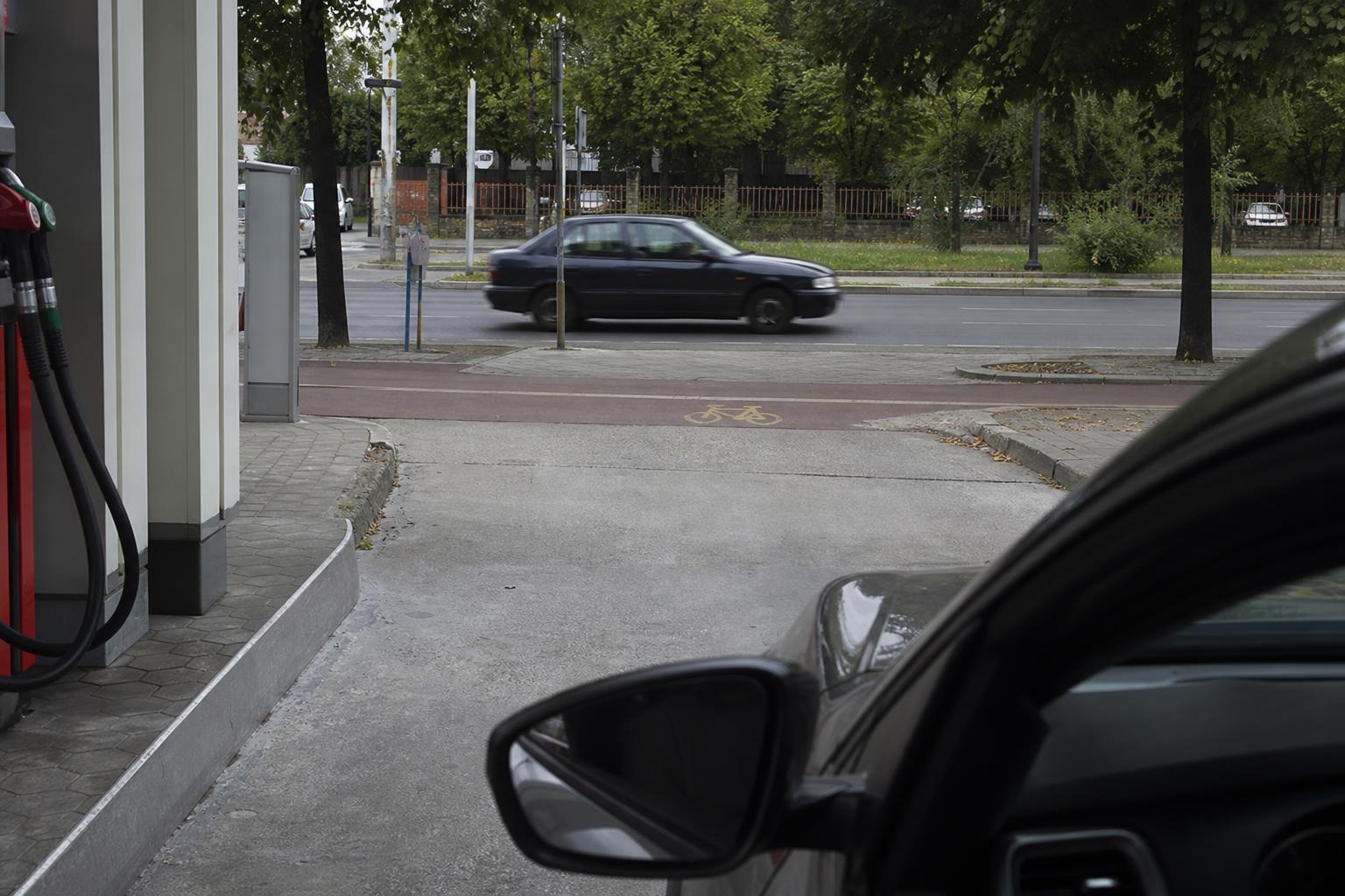 Autó hajt ki egy benzinkút kijáratánál a járdát és kerékpárutat keresztezve