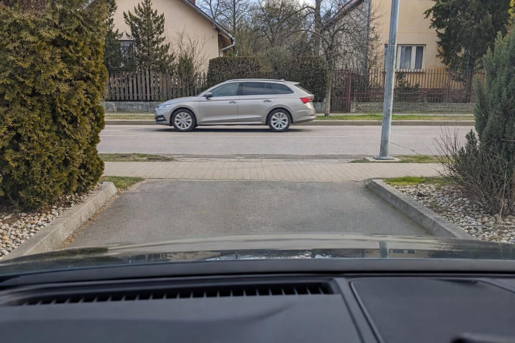 Autó várakozik egy magánút közútra történő kihajtásánál, elsőbbséget adva az úton haladóknak