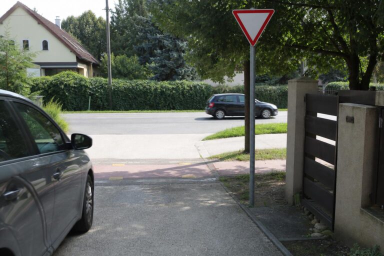 Autó hajt ki egy magánútról közútra elsőbbségadás kötelező tábla és járda mellett
