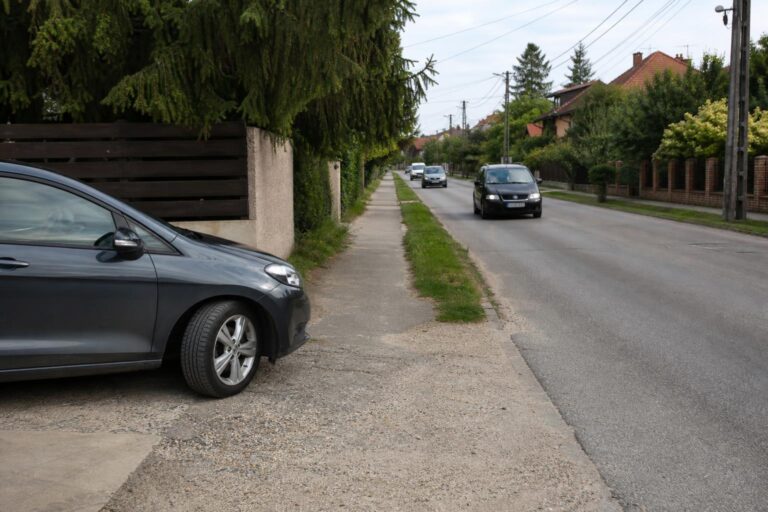 Autó hajt ki egy magánparkolóból a közútra, miközben a járdára és a közeledő forgalomra figyel
