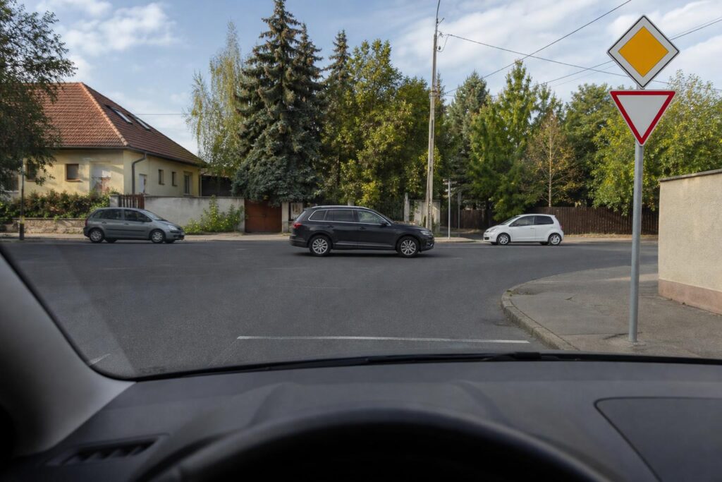 Magyarországi útkereszteződés elsőbbségi táblákkal és különböző irányból érkező autókkal