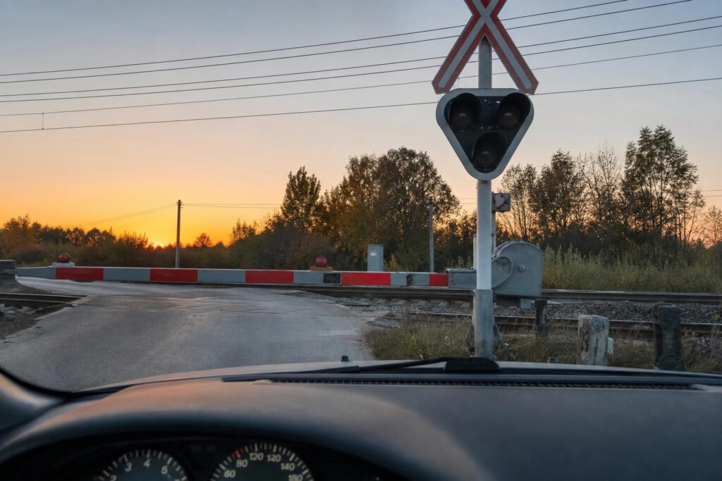 Autó műszerfalából látható vasúti átjáró hibás fénysorompóval és leengedett sorompórúddal