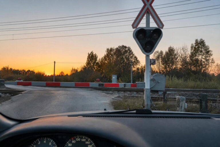 Autó műszerfalából látható vasúti átjáró hibás fénysorompóval és leengedett sorompórúddal