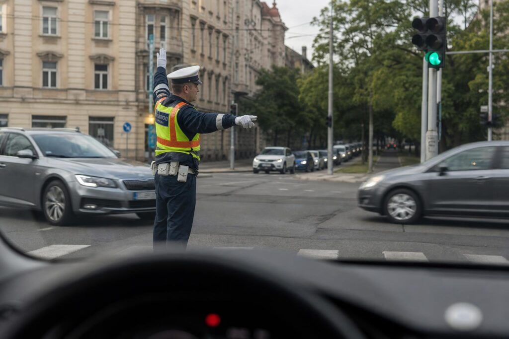 Forgalomirányító rendőr oldalról látható egy városi kereszteződésben, miközben a járművek biztonságosan haladnak