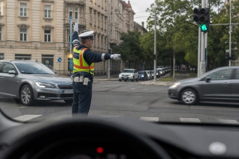 Forgalomirányító rendőr oldalról látható egy városi kereszteződésben, miközben a járművek biztonságosan haladnak