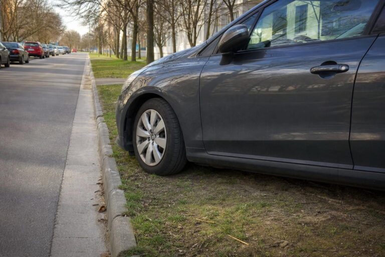 Autó füves út menti zöldsávon egy burkolt utca mellett