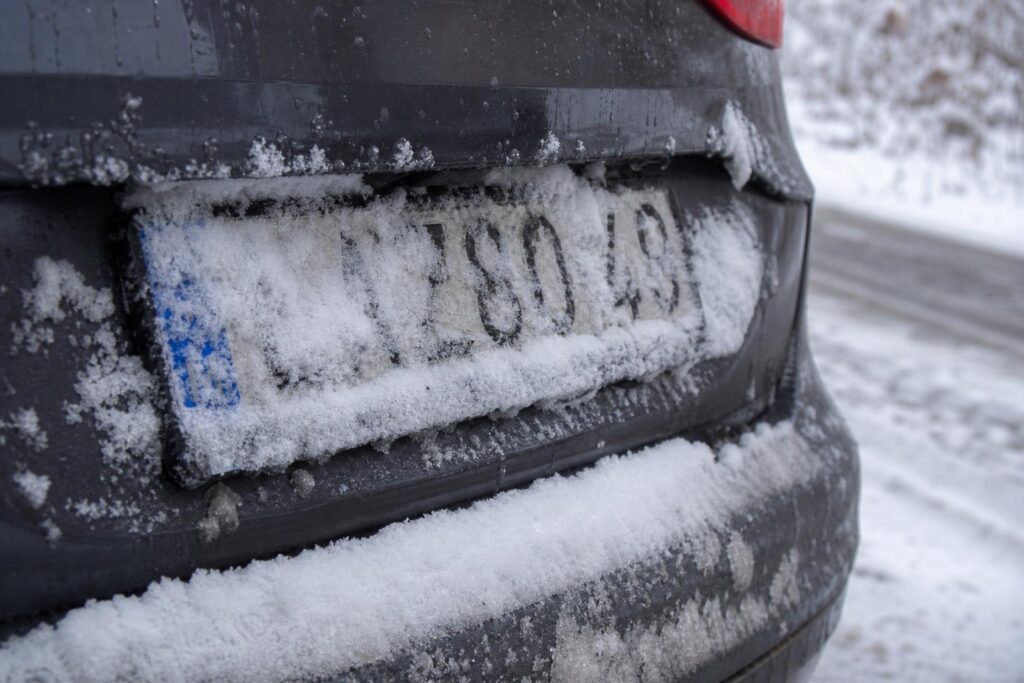 Hóval és latyakkal részben borított autós rendszámtábla téli út mellett