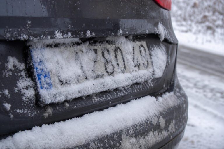 Hóval és latyakkal részben borított autós rendszámtábla téli út mellett