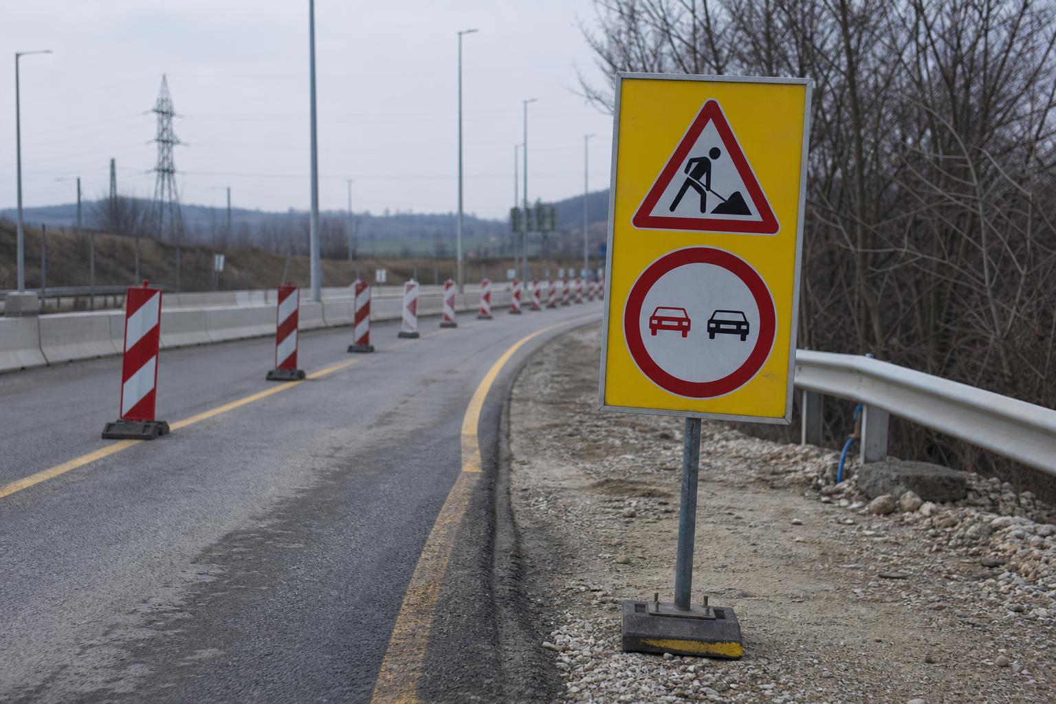Sárga hátterű ideiglenes közlekedési tábla útépítési terelés és forgalmi kúpok mellett