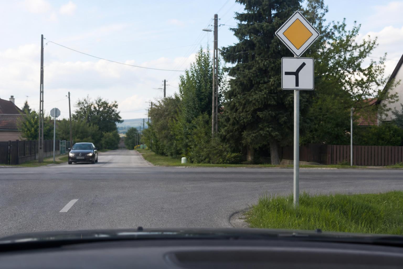 Kanyarodó főútvonalat jelző tábla egy kereszteződésben, jobbra ívelő főúttal