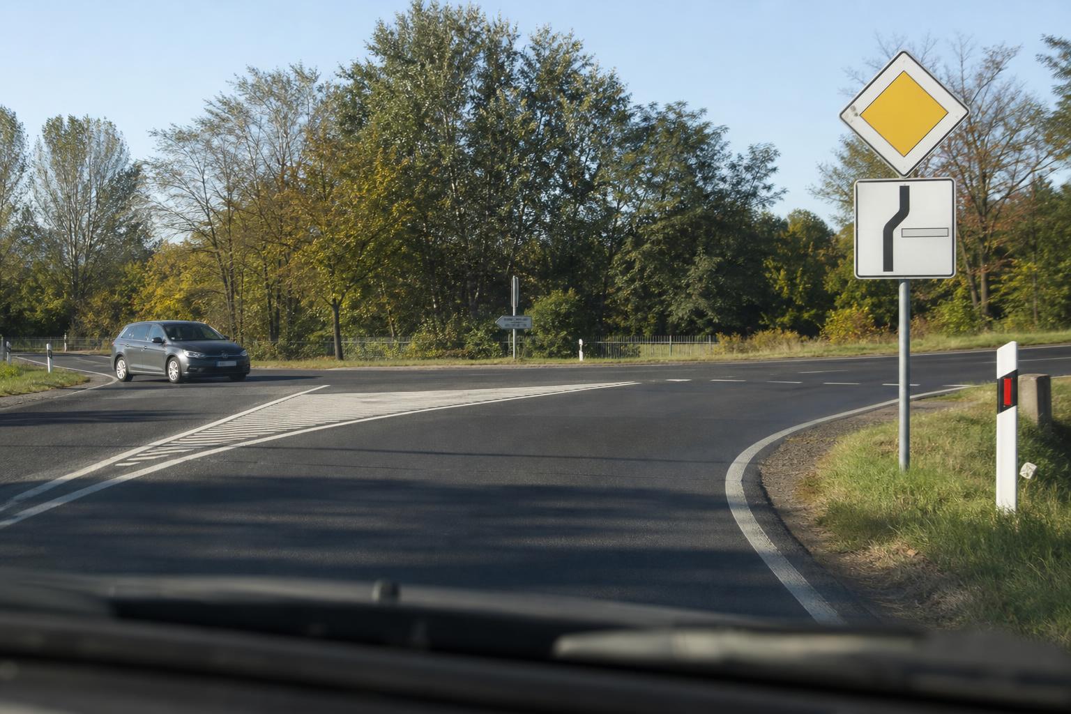 Kanyarodó főútvonalat jelző tábla és mellékútról érkező autó egy kereszteződésben