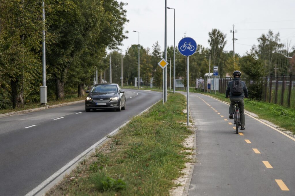 Párhuzamos úttest és kijelölt kerékpárút, amelyen kerékpáros közlekedik egy autó mellett