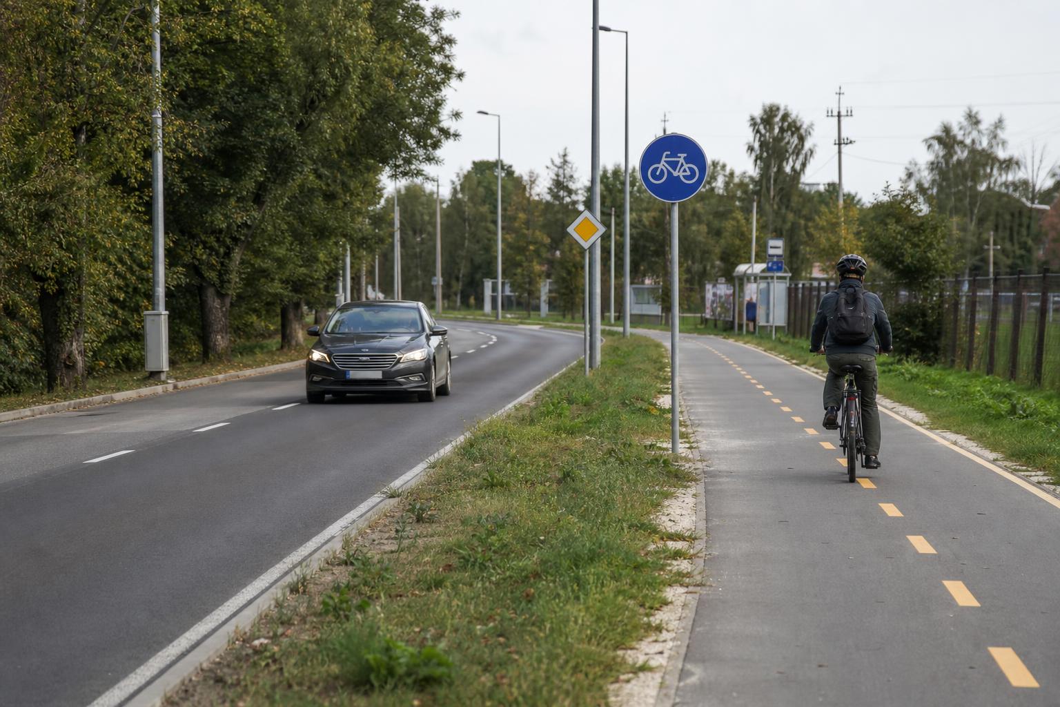 Párhuzamos úttest és kijelölt kerékpárút, amelyen kerékpáros közlekedik egy autó mellett
