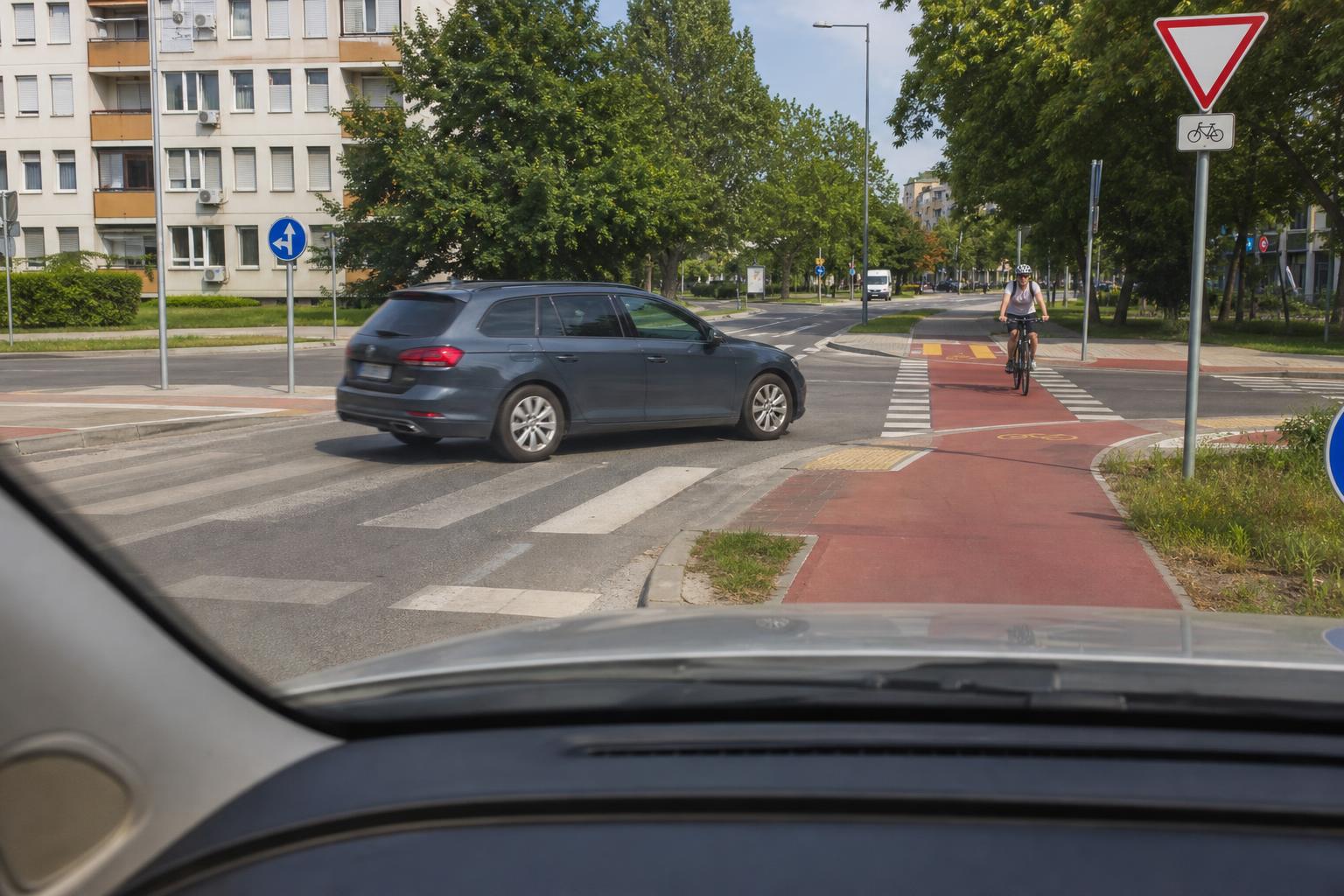 Autó kerékpárutat keresztez egy városi csomópontban, jól látható táblákkal és útburkolati jelekkel