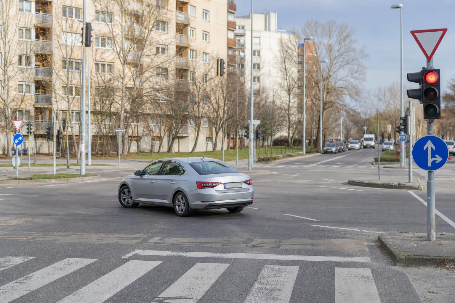 Autó szabályos megfordulása egy jól belátható kereszteződésben, útburkolati jelekkel és gyalogos-átkelőhellyel