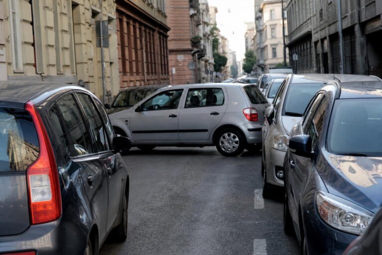Második sorban megálló autó szabályosan parkoló járművek mellett, forgalmi akadályt okozva egy városi utcában