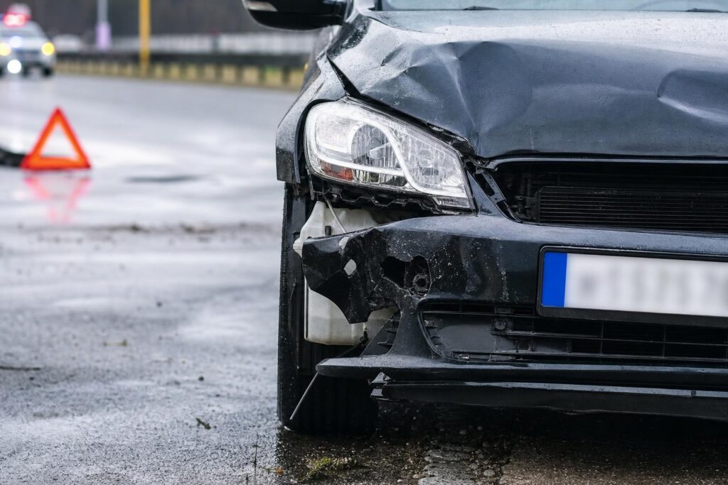 Közúti balesetben sérült autó az úttesten, mellette elakadásjelző háromszöggel