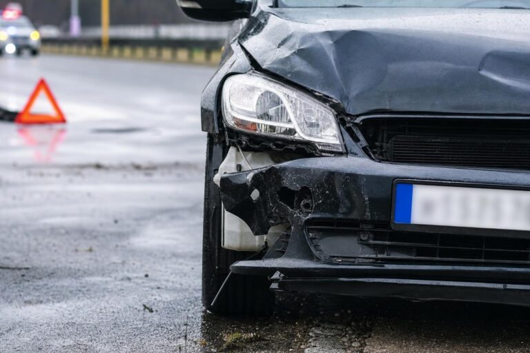 Közúti balesetben sérült autó az úttesten, mellette elakadásjelző háromszöggel