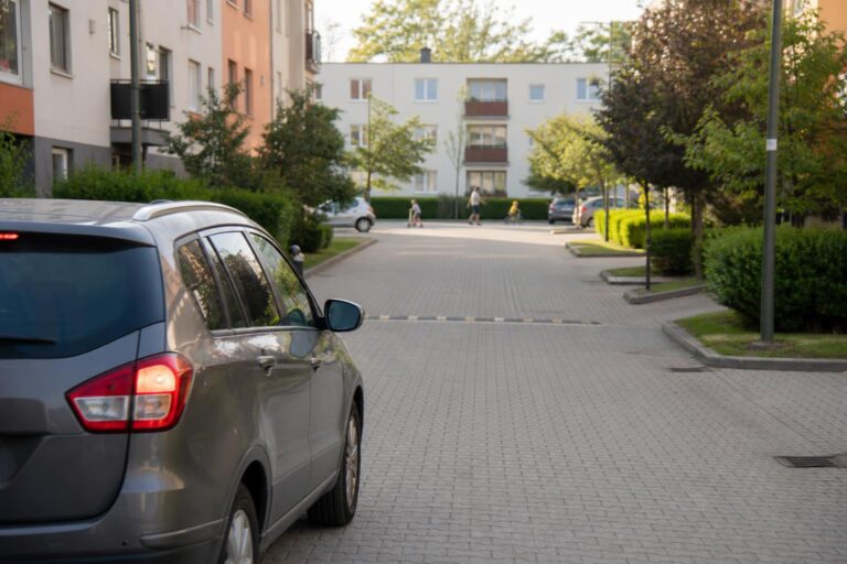 Lakó-pihenő övezetben lassan haladó autó és az úttestet használó gyalogosok