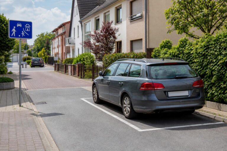 Autó kijelölt parkolóhelyen egy lakó-pihenő övezetben, a területet jelző közlekedési táblával