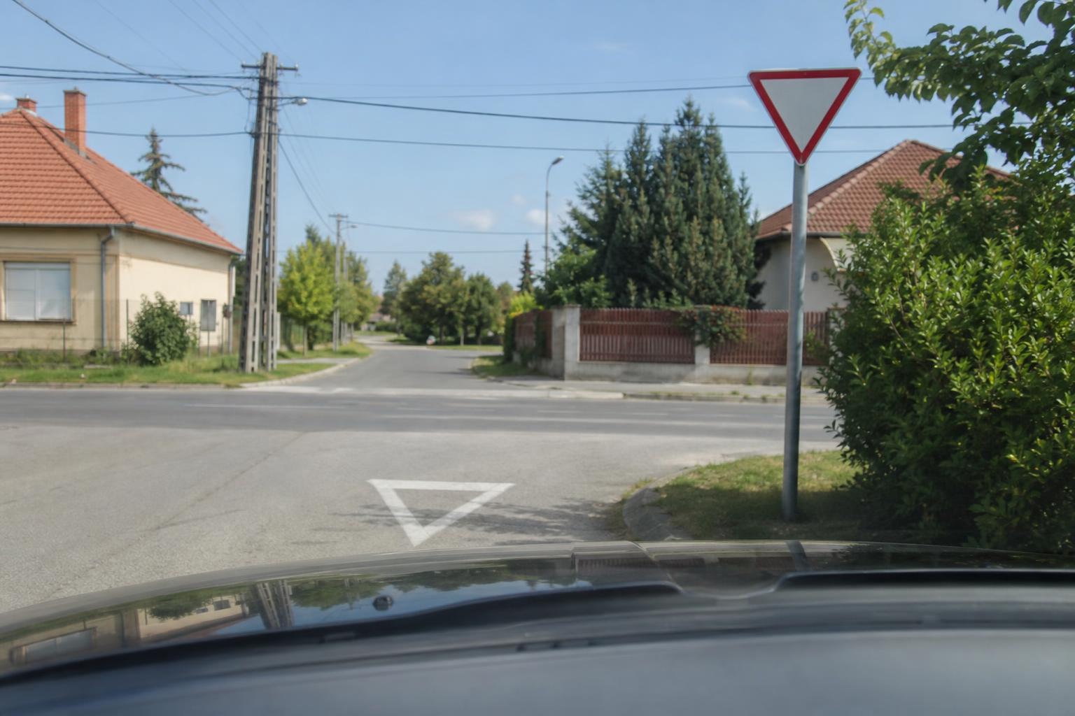 Autó közeledik a macisajt táblával jelzett kereszteződéshez