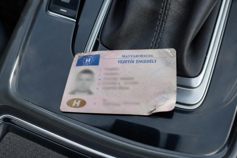 Megrongálódott magyar vezetői engedély sérült sarkával egy autó középkonzolján