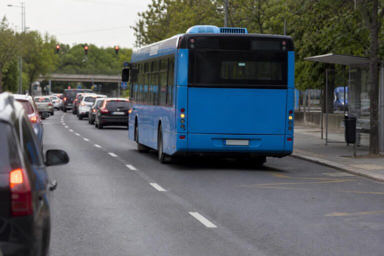 Menetrend szerint közlekedő városi busz sávváltása egy magyarországi úton, buszsáv és útburkolati jelek mellett