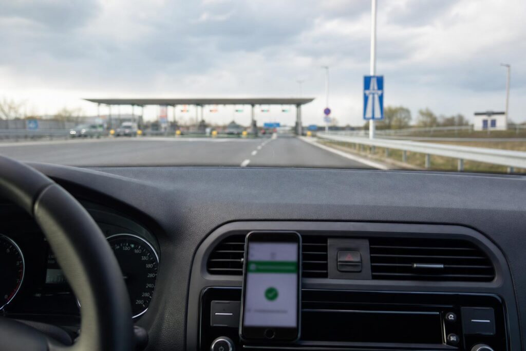 Autó a magyar autópálya felhajtója előtt, az úthasználati matrica megvásárlására utaló telefonnal a középkonzolon