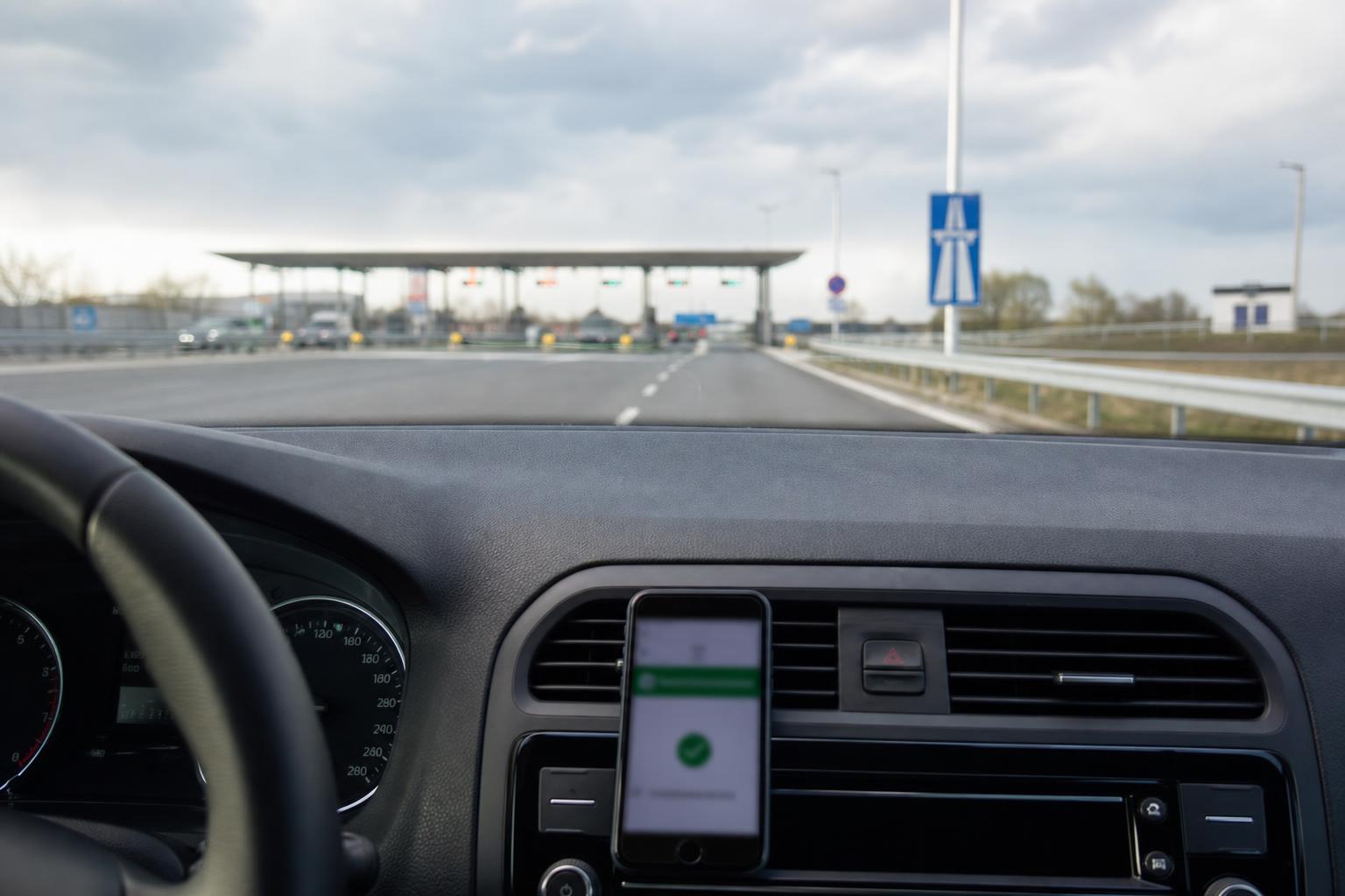 Autó a magyar autópálya felhajtója előtt, az úthasználati matrica megvásárlására utaló telefonnal a középkonzolon