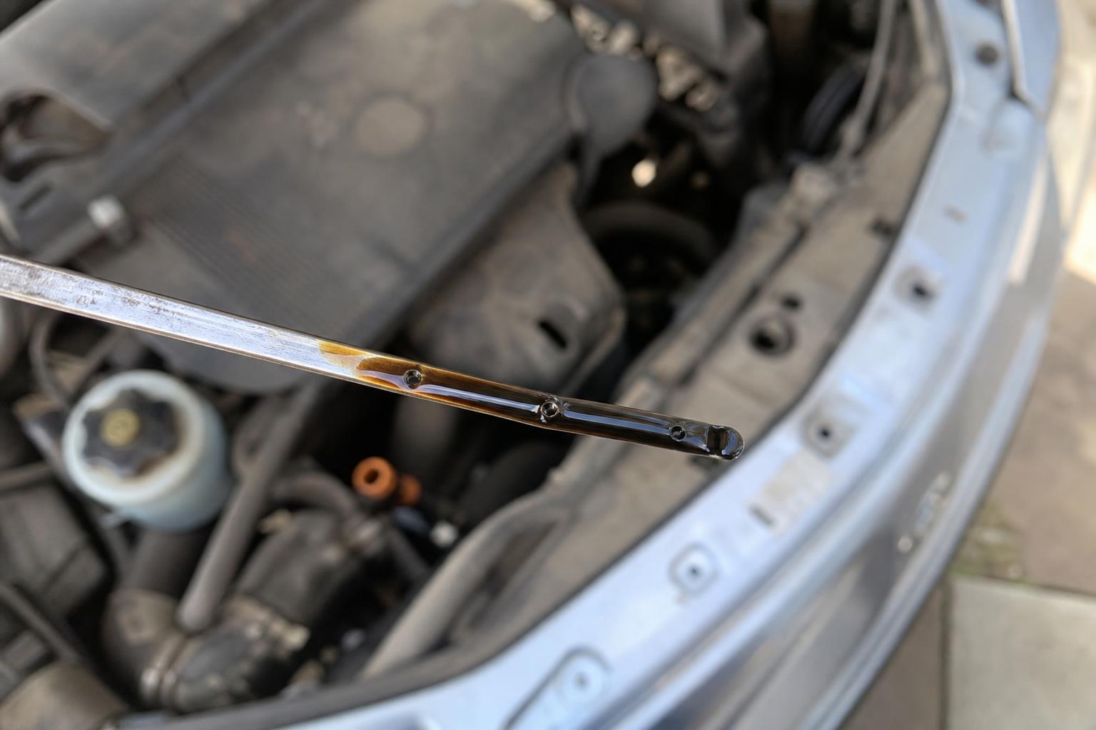 Használt autó motorjának nívópálcája sötét motorolajjal ellenőrzés közben