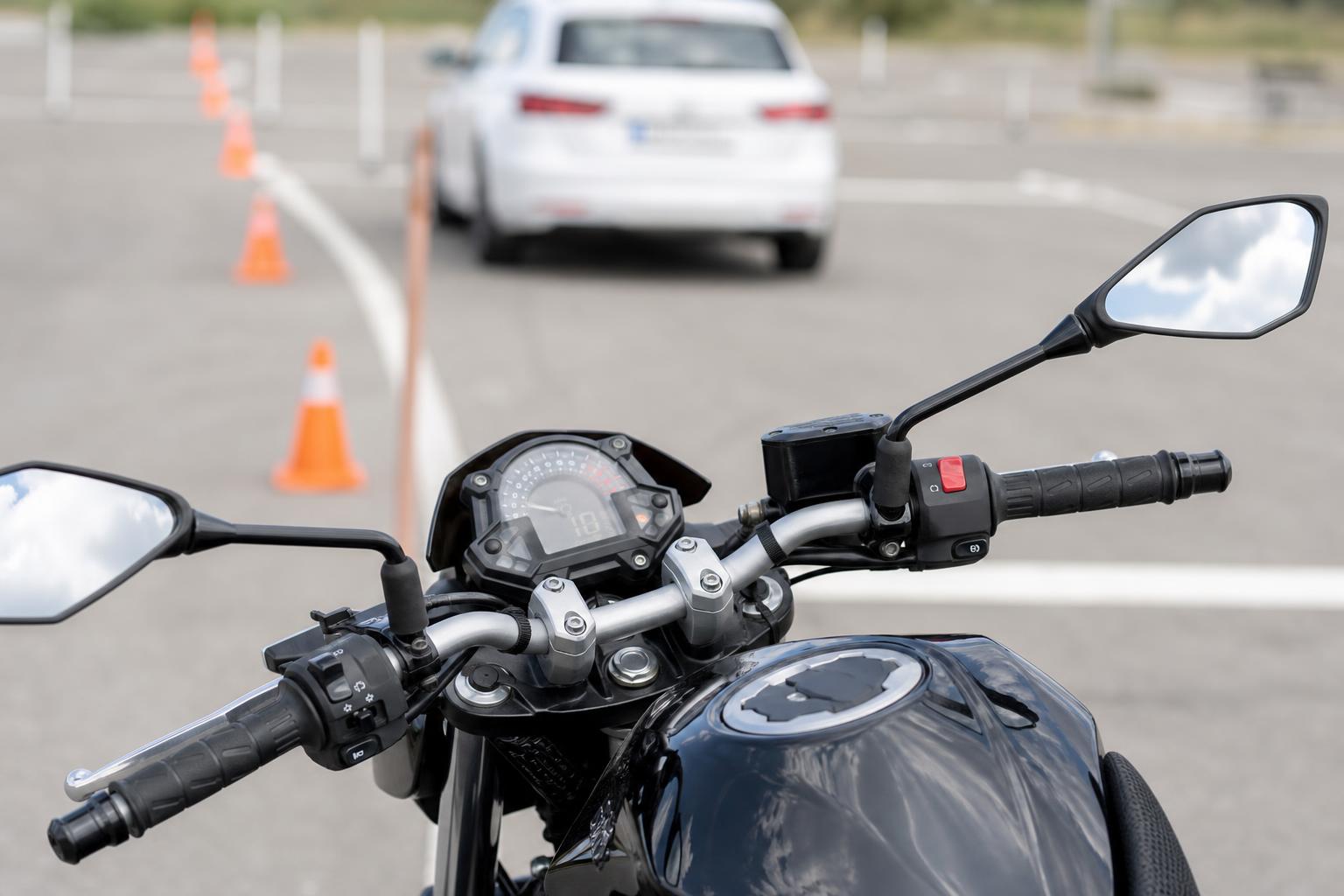 Motorkerékpár kormánya és műszerfala forgalmi vizsga közben, a háttérben elmosódott vizsgaútvonallal