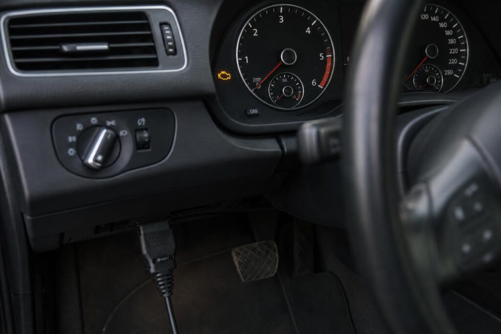 Használt autó műszerfala világító motorhiba-jelzéssel és csatlakoztatott OBD-diagnosztikai eszközzel
