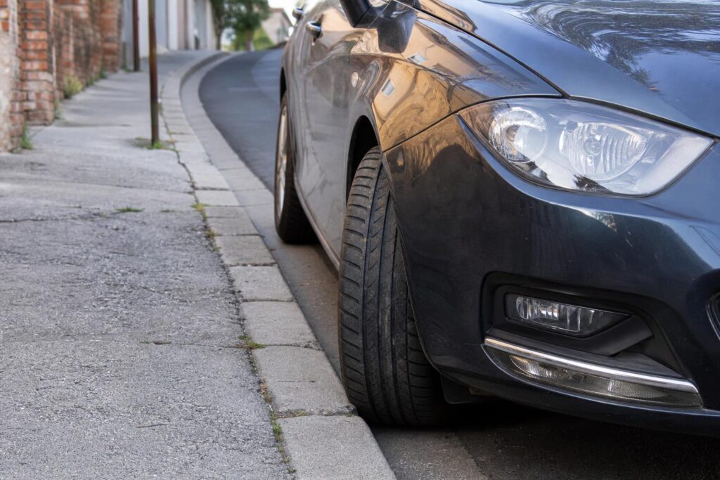 Parkoló autó lejtős úton, a járdaszegély felé fordított kerekekkel