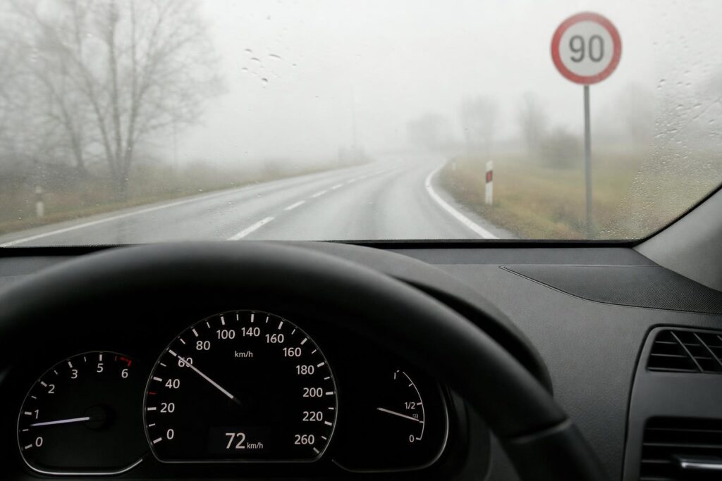 Autó műszerfala mérsékelt sebességet mutat ködös, nedves úton, a megengedett sebességhatár alatt