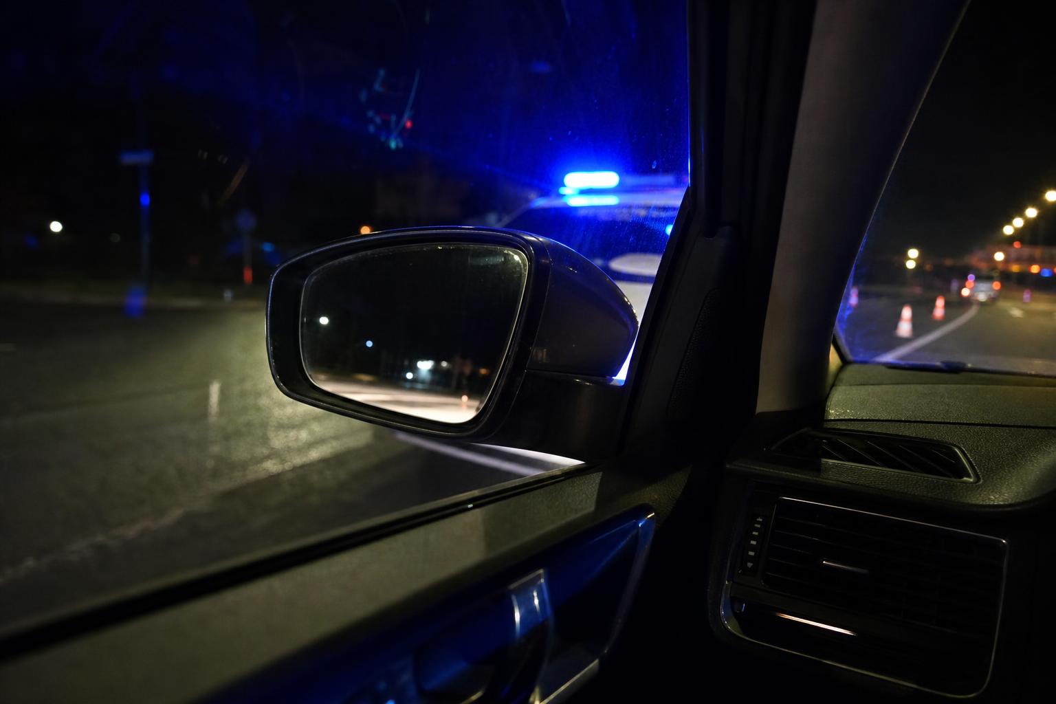 Megállított autó rendőri ellenőrzésnél, a visszapillantóban és az ablakon tükröződő kék fényekkel