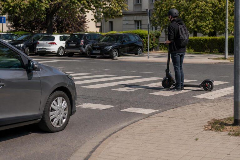 Autó lassít a zebránál, miközben a rolleres a rollert tolva készül átkelni