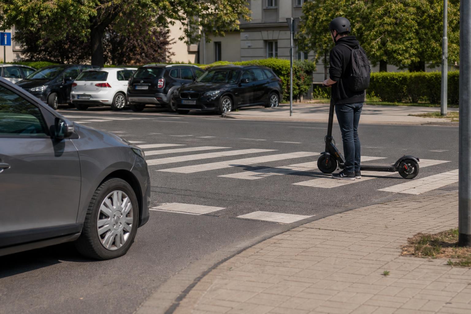 Autó lassít a zebránál, miközben a rolleres a rollert tolva készül átkelni