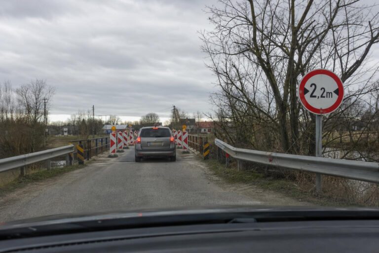 Autó közeledik keskeny útszakaszt jelző szélességkorlátozó táblához