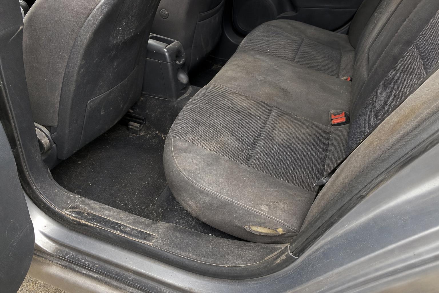 Erősen kopott hátsó ülés és ajtóküszöb egy taxi múltú használt autó utasterében