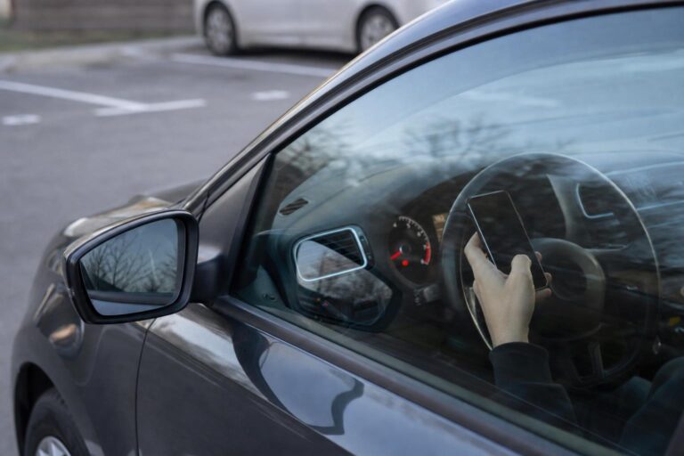 Kézben tartott mobiltelefon egy szabályosan parkoló, járó motorú autó vezetőülésénél