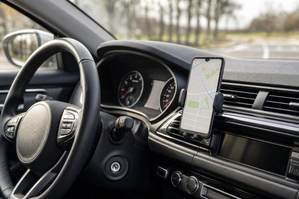 Rögzített mobiltelefon és kormány egy autó belsejében, kihangosított navigáció használatára utaló beállítással
